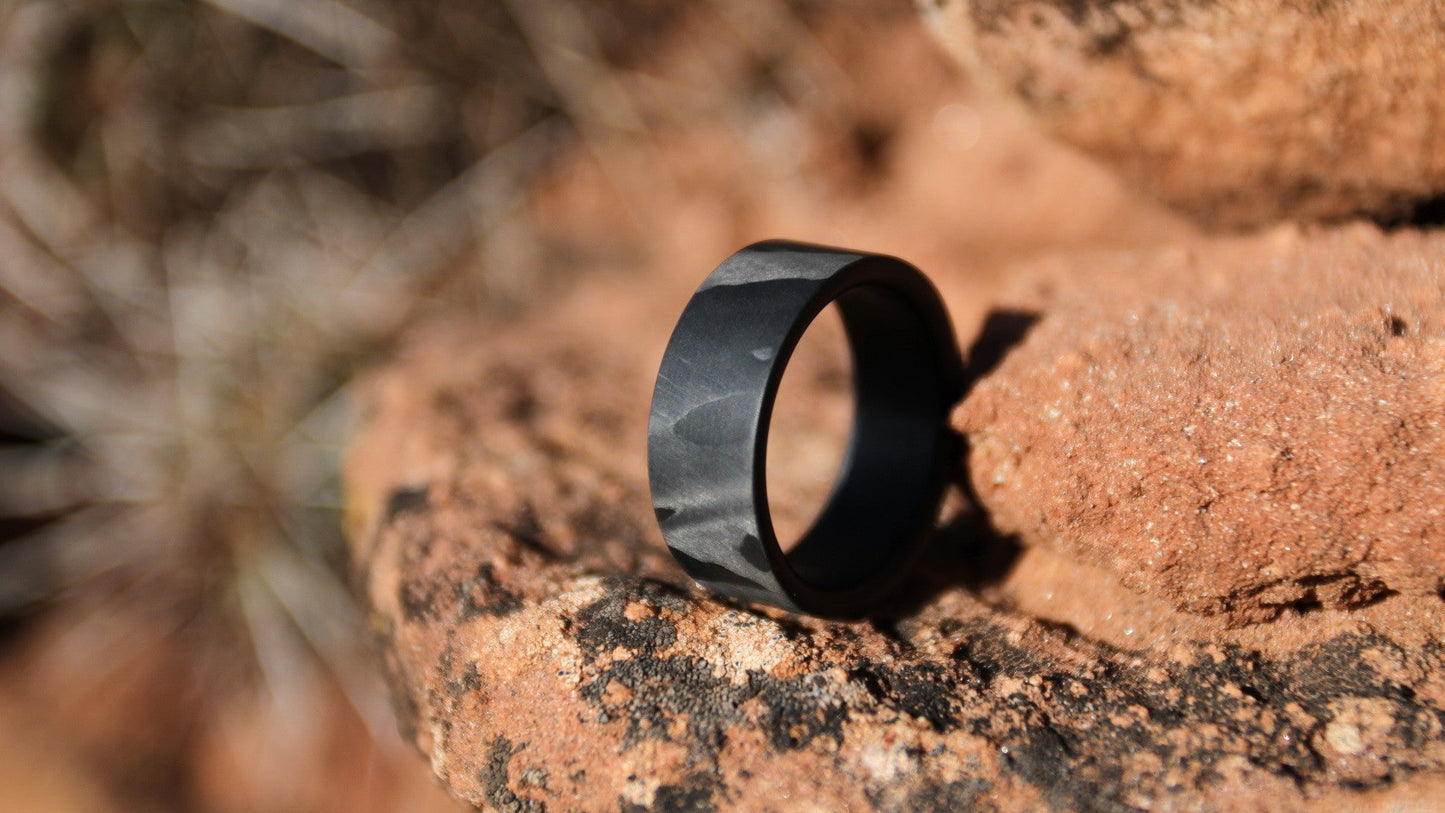 Matte carbon fiber ring with marbled patterns resting on natural rock